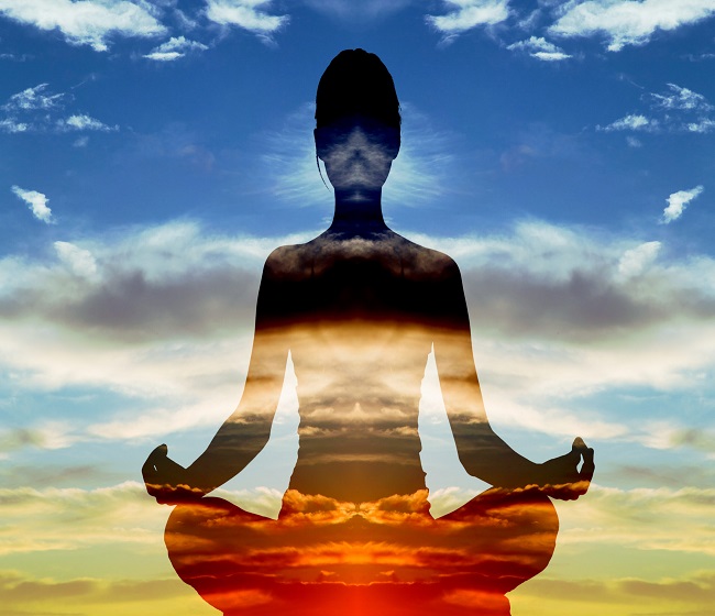 Silhouette of woman doing yoga in lotus position over sunset sky. Concept of connection with the universe and nature